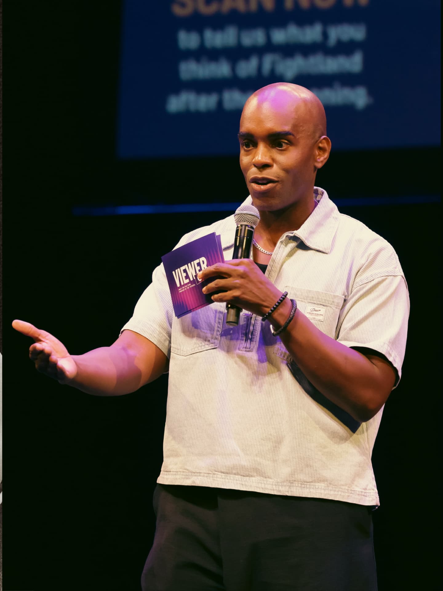 Host on stage holding a ViewerCon 2026 program